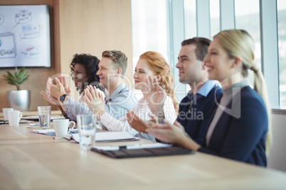 Happy business people clapping at conference table during meeting