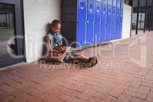 Full length of elementary student using mobile phone while sitting by lockers