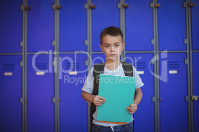 Portrait of boy holding books against lockers