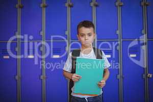 Portrait of boy holding books against lockers