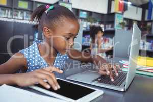 Girl using tablet computer and laptop in library