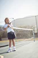 Girl holding tennis racket while sitting by net
