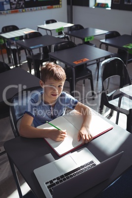 Smiling boy with laptop and book at desk
