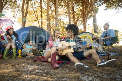 Young woman with male friend playing guitar at campsite Young woman with male friend playing guitar at campsite