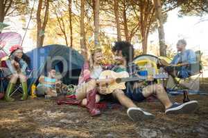 Young woman with male friend playing guitar at campsite