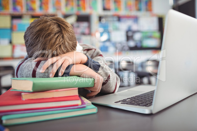 Tired schoolboy resting on stack of in classroom