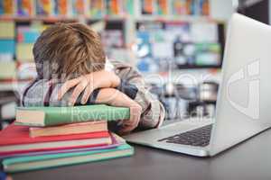 Tired schoolboy resting on stack of in classroom