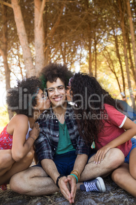 Females kissing young male friends sitting on field