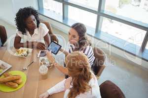 Female business colleagues discussing over digital tablet around breakfast table