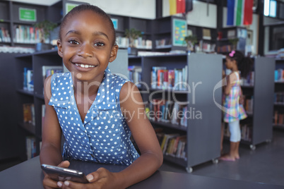 Smiling girl with mobile phone at desk in library