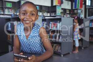 Smiling girl with mobile phone at desk in library