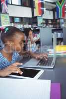 Girl using digital tablet and laptop in library