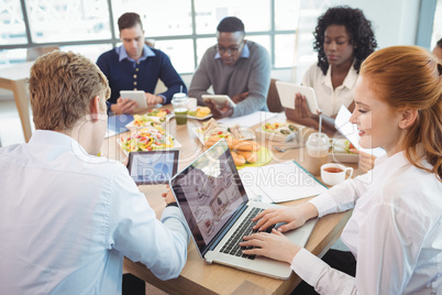 Business colleagues using laptop and digital tablets around breakfast table