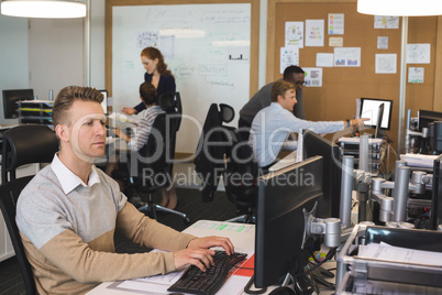 Young businessman typing on keyboard while colleagues working in background
