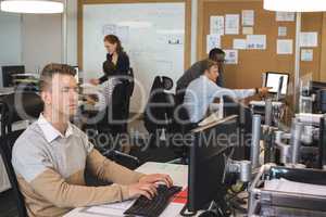 Young businessman typing on keyboard while colleagues working in background