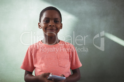 Smiling boy holding cellphone against greenboard