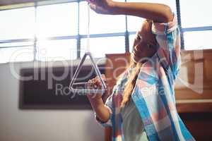 Portrait of girl playing triangle in classroom