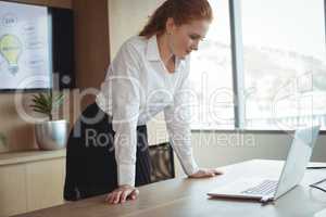 Young businesswoman looking at laptop while leaning on desk