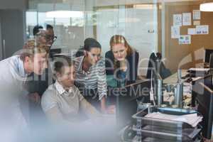 Businessman discussing with colleagues while working on computer seen through glass