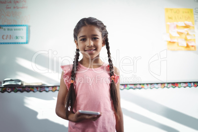 Girl holding mobile phone while standing against wall