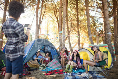 Man photographing smiling friends at campsite