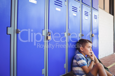 Boy talking on mobile phone while sitting by lockers