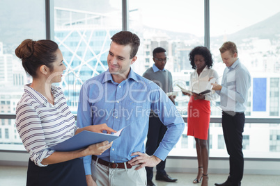 Smiling business colleagues discussing with team in background