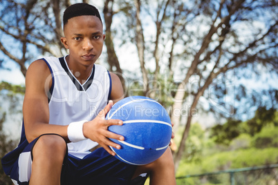 Portrait of male teenager with ball sitting on bench