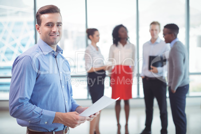 Smiling businessman holding documets with colleagues standing in background