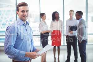 Smiling businessman holding documets with colleagues standing in background