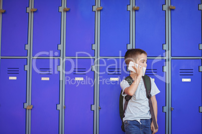 Elementary boy talking on mobile phone against lockers