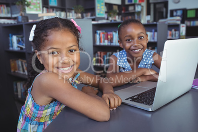 Smiling girls with laptop at desk in library