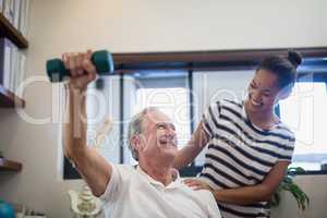 Smiling senior male patient lifting dumbbell while looking at female doctor