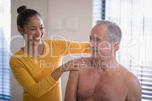 Smiling female therapist giving neck massage to shirtless senior male patient at hospital ward