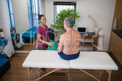 High angle view of smiling female therapist looking at shirtless senior male patient sitting on bed High angle view of smiling female therapist looking at shirtless senior male patient sitting on bed