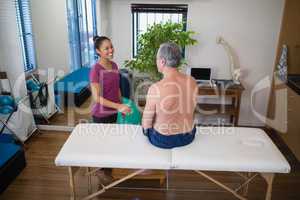 High angle view of smiling female therapist looking at shirtless senior male patient sitting on bed