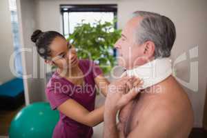 Female therapist examining neck collar of senior male patient