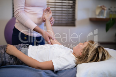 Midsection of female therapist examining arm with boy lying on bed