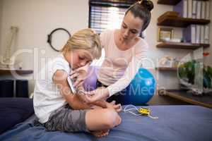 Young female therapist positioning electrodes on arm of boy