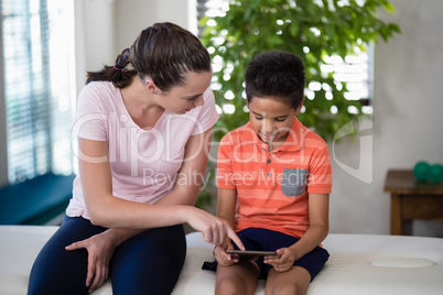 Boy looking while female therapist pointing at digital tablet