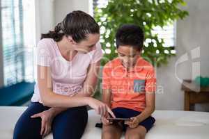 Boy looking while female therapist pointing at digital tablet