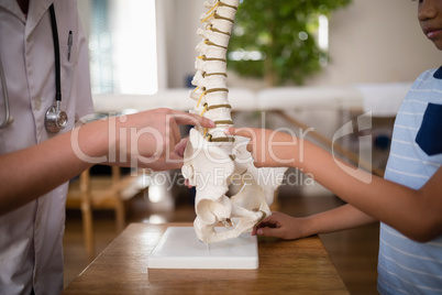 Midsection of female therapist and boy pointing at artificial spine on table