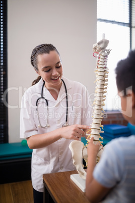 Smiling female therapist explaining boy while pointing at artificial spine