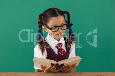 Schoolgirl reading book against chalkboard