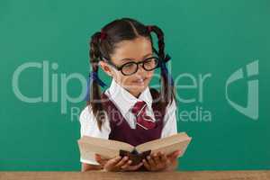 Schoolgirl reading book against chalkboard