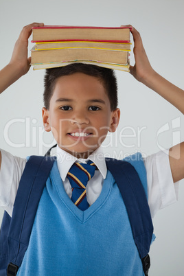 Schoolboy holding books on his head against white background