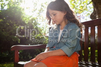 Sad girl sitting on wooden bench against plants