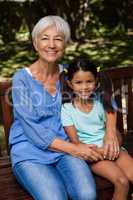 Portrait of granddaughter and senior woman sitting on wooden bench