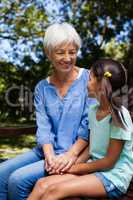 Smiling granddaughter and grandmother holding hands while sitting on bench