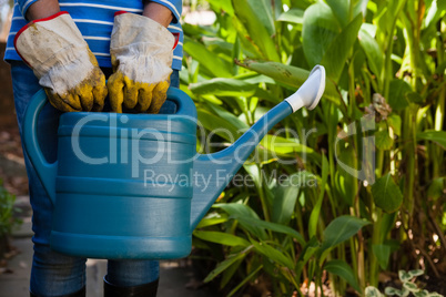 Midsection of senior woman standing with watering can against plants